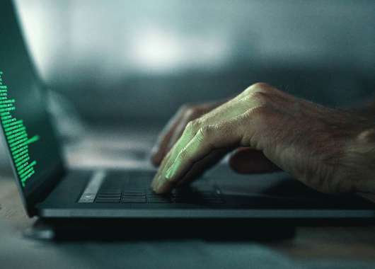 Side view of two hands typing on a laptop with green code.
