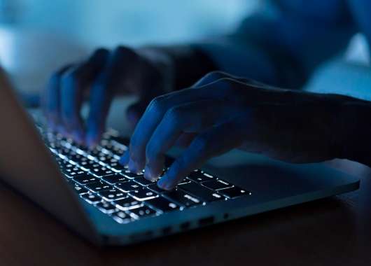 A figure of a dark web surfer using a laptop to access the dark web.