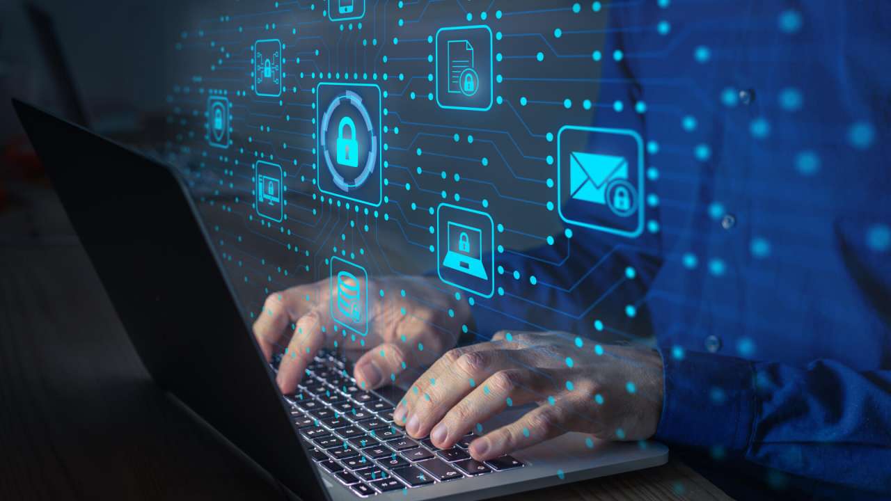 A person typing on their laptop with digital security symbols projecting in front of them