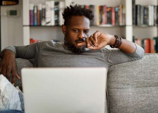 Photo of a man sitting on a couch and looking at a laptop