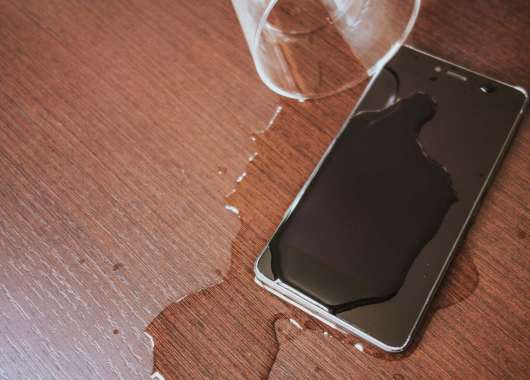 Smartphone on a table covered with water next to a spilled cup of water.