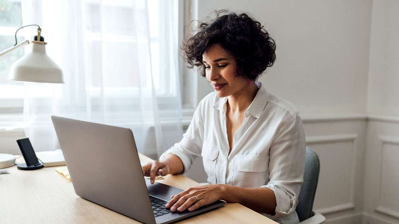 Woman sitting at table and typing on a laptop.