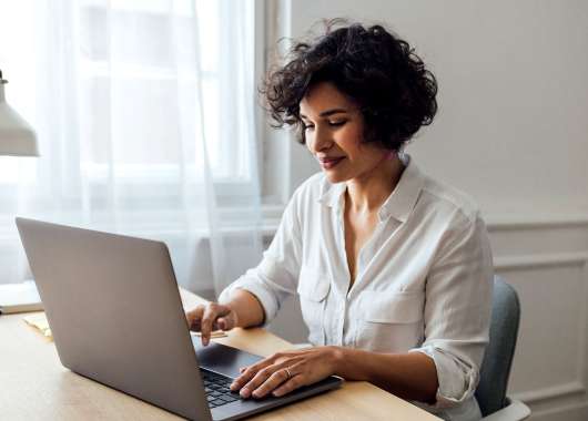 Woman sitting at table and typing on a laptop.