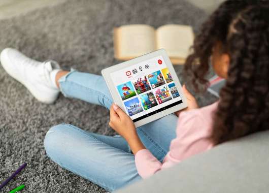A child sits on the floor of their house against a couch while using YouTube Kids on their tablet