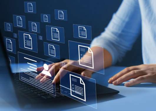 Hands of a man typing on a computer while icons of digital files hang over the laptop.