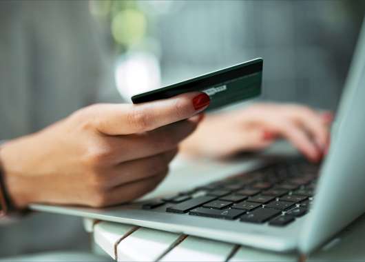 Hand holding a credit card next to a laptop.