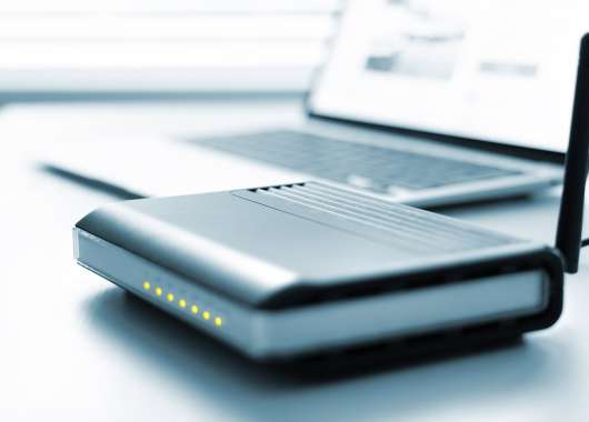 Small grey router sitting in front of a laptop.